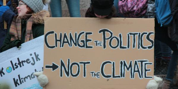 A person holds a big cardboard sign that says "Change the Politics Not the Climate". Photo by Tania Malréchauffé on Unsplash